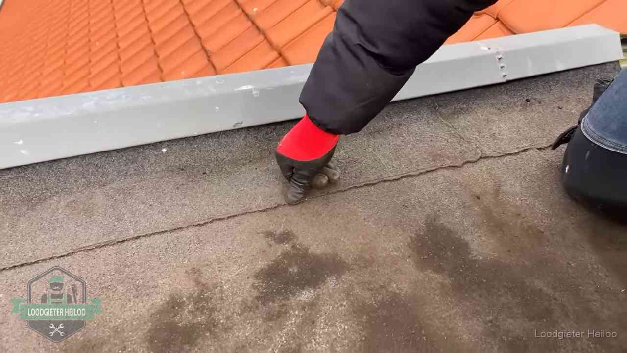 Vakman wijst een naad met vochtplekken aan op een bitumen plat dak in Heiloo