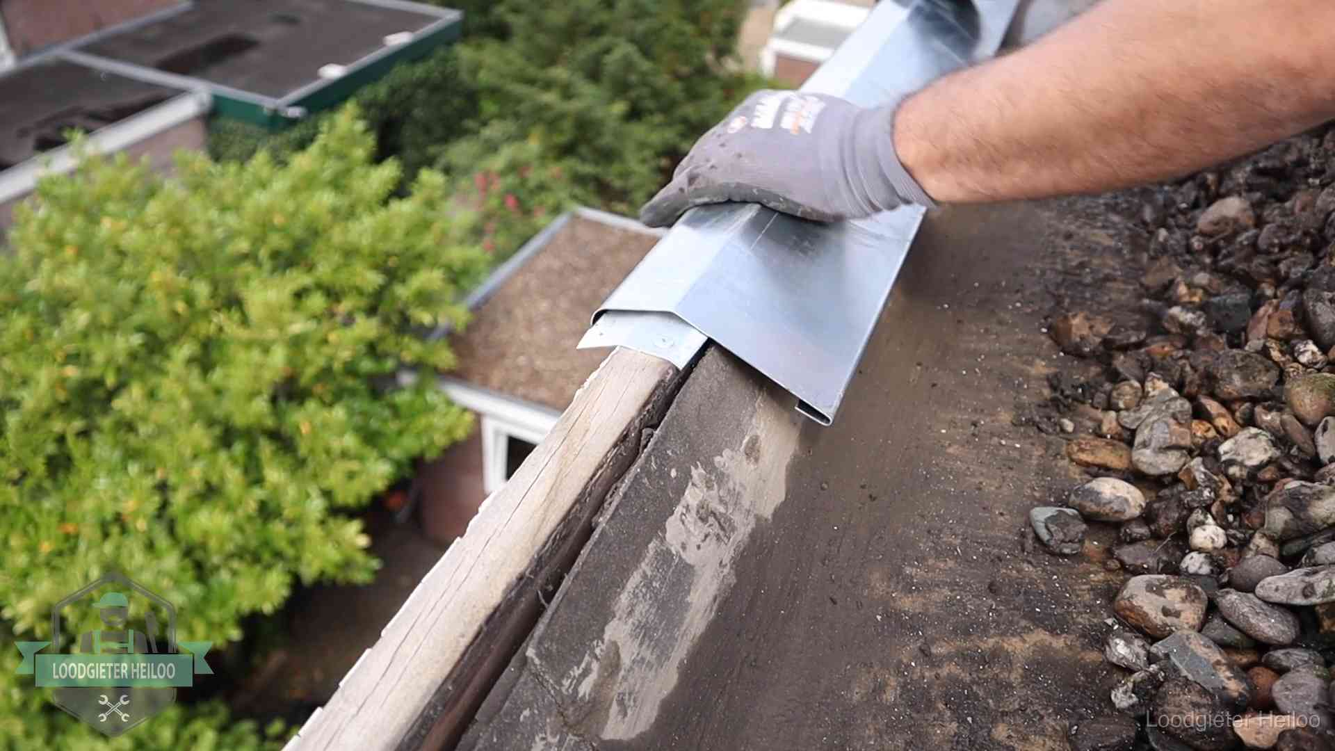 Dakdekker plaatst een zinken deklijst op een dakrand met uitzicht over een woonwijk in Heiloo