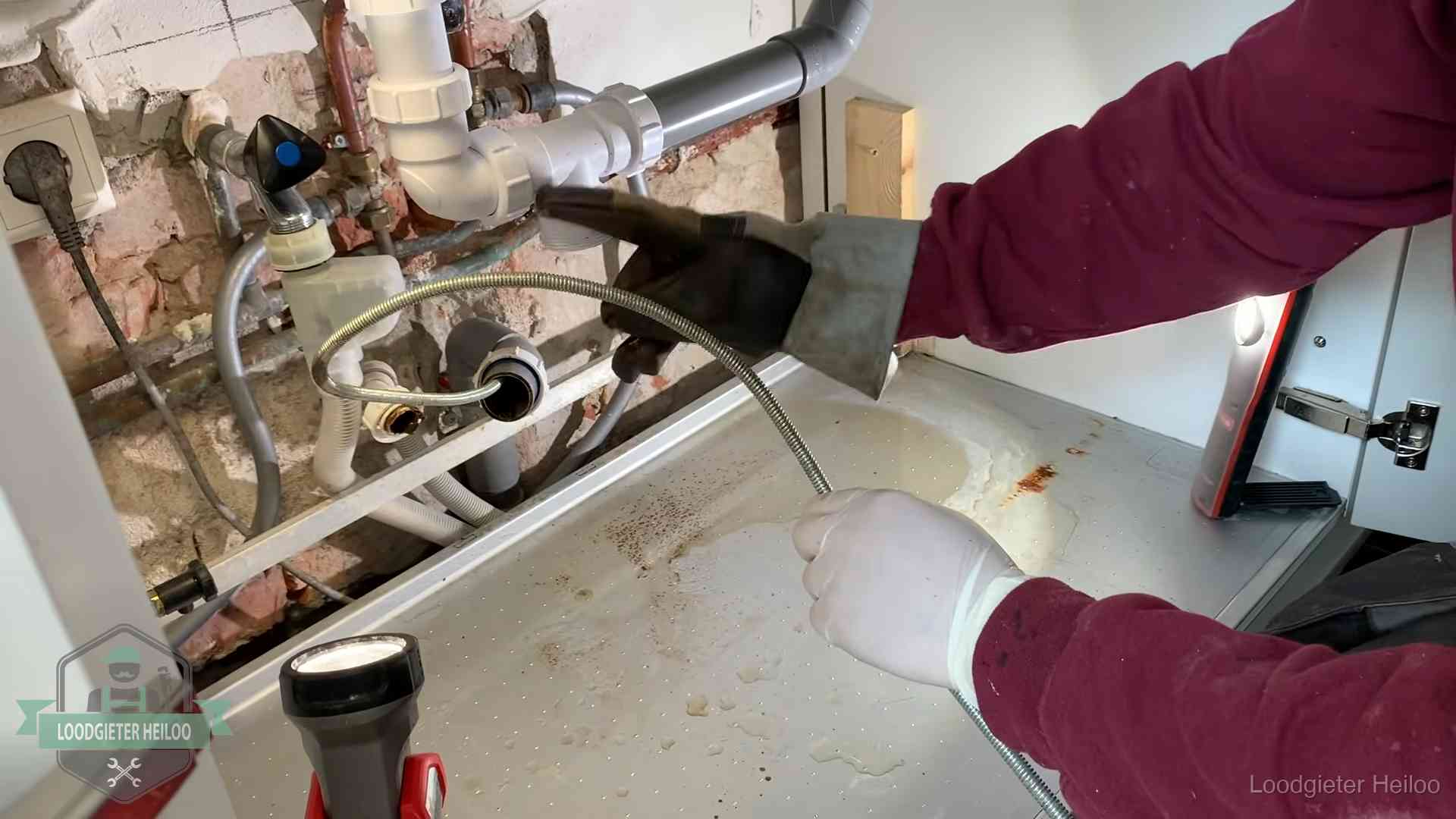 Ontstoppingsveer gaat in een geopende sifonaansluiting onder het aanrecht in Heiloo