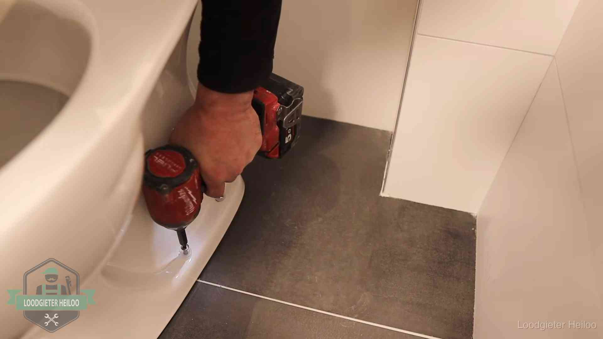 Kosten wc ontstoppen in Heiloo Loodgieter zet de voet van een wc-pot vast op de tegelvloer in Heiloo